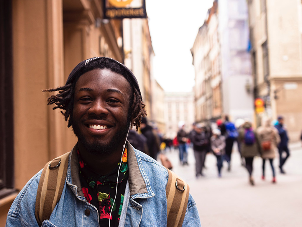 Student with backpack and headphones smiling on a busy street