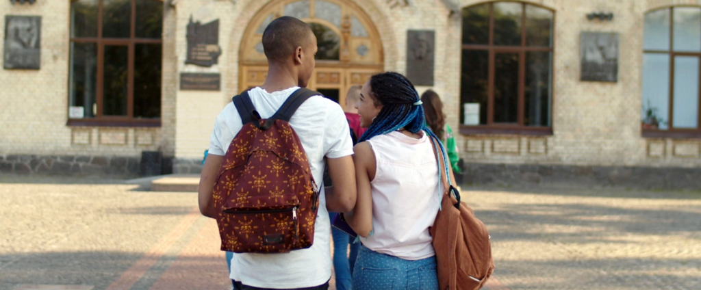 Two African American students with backpacks standing next to each other talking outside of a college campus building.