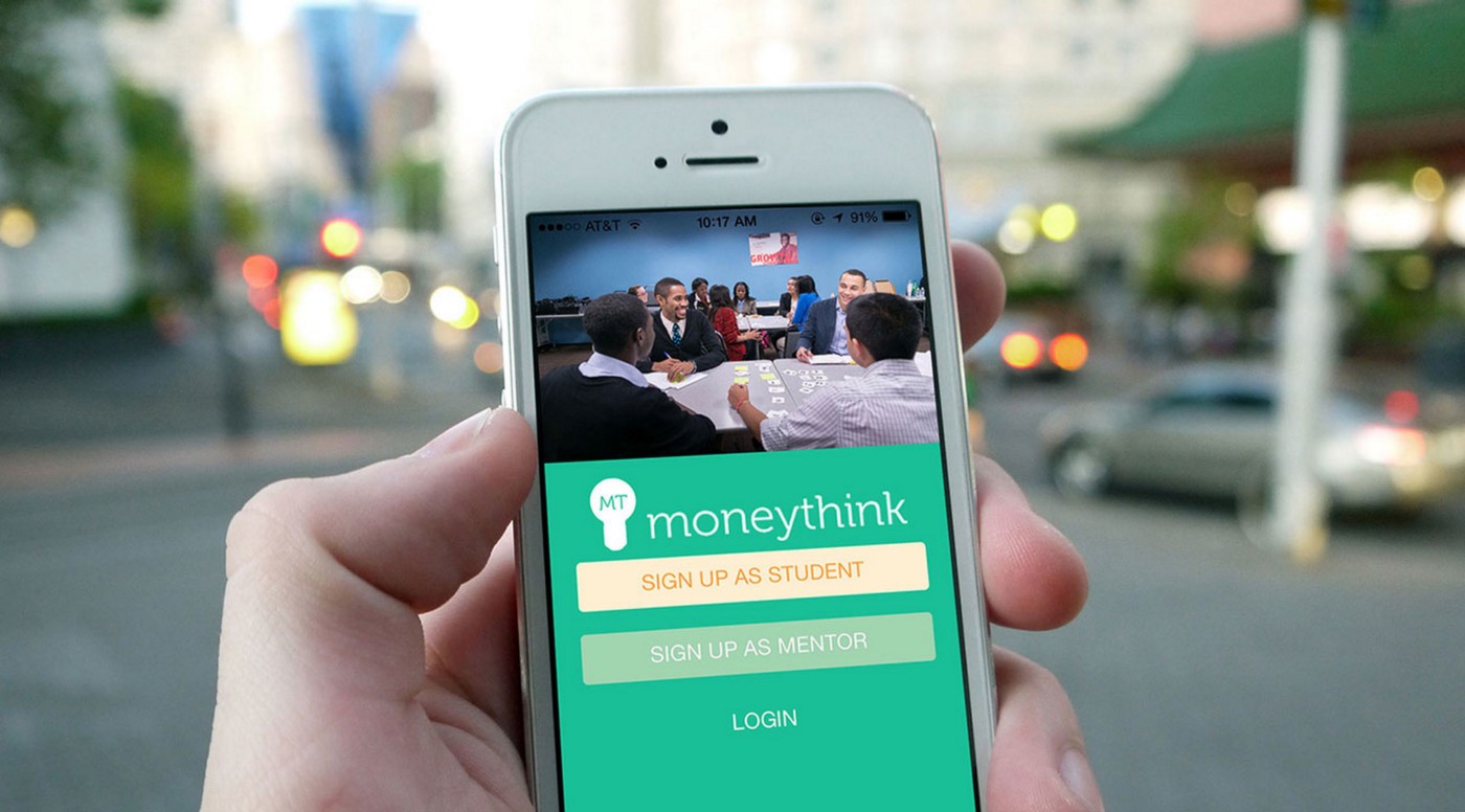 Student holds mobile device with Moneythink app on the screen.